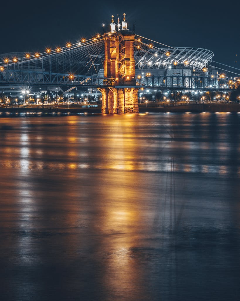 A stunning view of the Roebling Bridge and cityscape illuminated at night with reflections on the river.